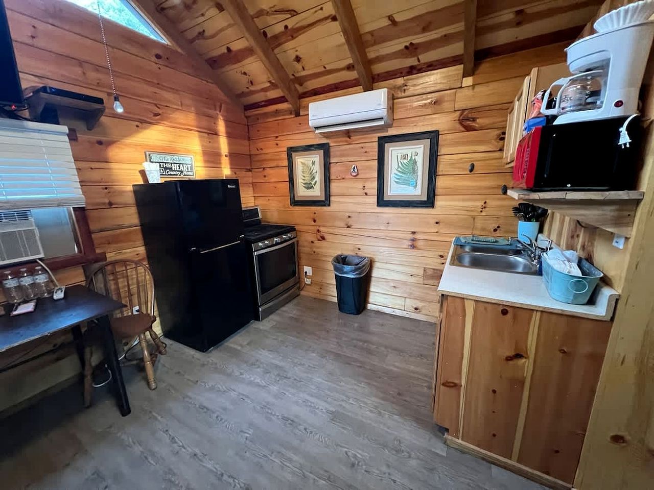 A compact kitchen with wooden walls, a stove, a sink, and a trash bin.