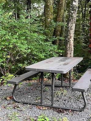 Une table de pique-nique avec des bancs, située dans un espace boisé.