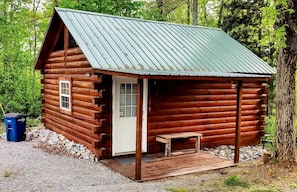 Une cabane en rondins avec un porche, une porte et un petit banc.