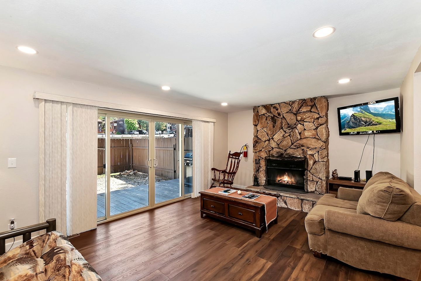 A living room with a stone fireplace, a sofa, a coffee table, and a television mounted on the wall.
