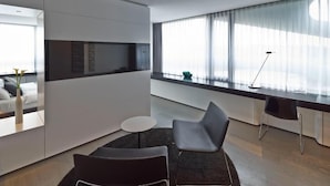 Une chambre moderne avec un canapé, une petite table ronde, un bureau et une grande fenêtre avec des rideaux.