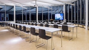 Une salle de conférence dotée de longues tables et de chaises, de grandes fenêtres et d’un écran de projection.