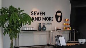 Un comptoir de restaurant avec une enseigne indiquant « SEVEN AND MORE Restaurant », une plante et une présentation de fruits.