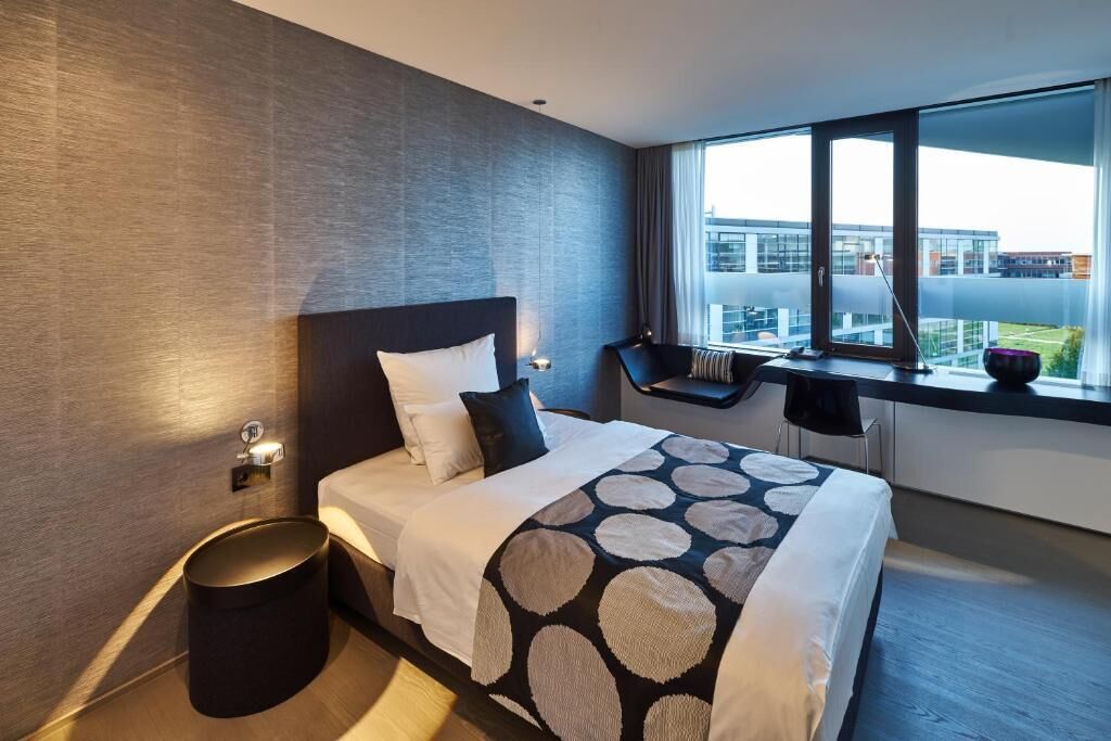 Une chambre d’hôtel moderne avec un grand lit, un petit bureau, une chaise et une fenêtre donnant sur la ville.