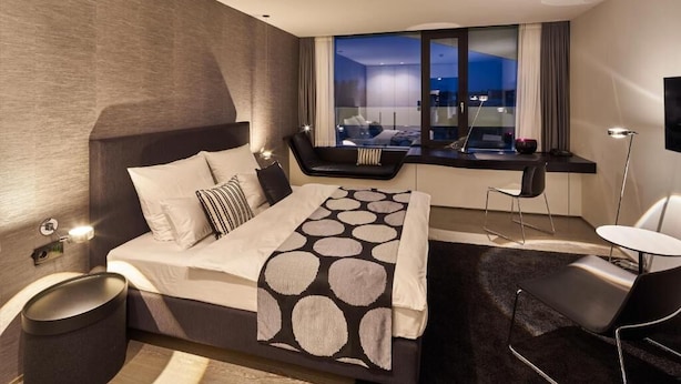 A modern hotel room with a large bed, a seating area with a view, and a small table.