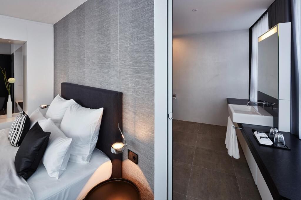 Una habitación de hotel moderna con cama, mesita de noche y baño con lavabo y espejo.