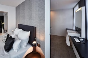 Una habitación de hotel moderna con cama, mesita de noche y baño con lavabo y espejo.