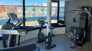 A gym with cardio machines, weight equipment, and large windows offering a view of buildings.