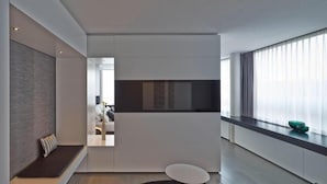 A modern hotel room with a sofa, a small round table, a TV, and a large window with curtains. - Campus at Home (Planegg)