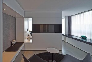 A modern hotel room with a sofa, a small round table, a TV, and a large window with curtains. - Campus at Home (Planegg)