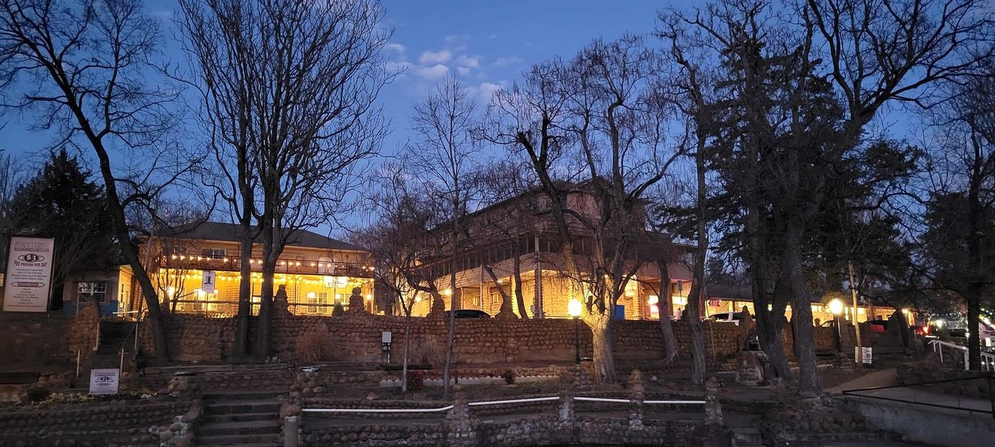 A historic building with stone walls and a balcony, surrounded by trees.