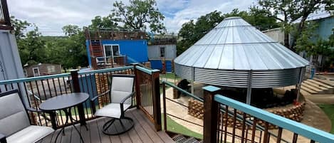 A wooden deck with outdoor furniture, a metal gazebo, and a blue building in the background.