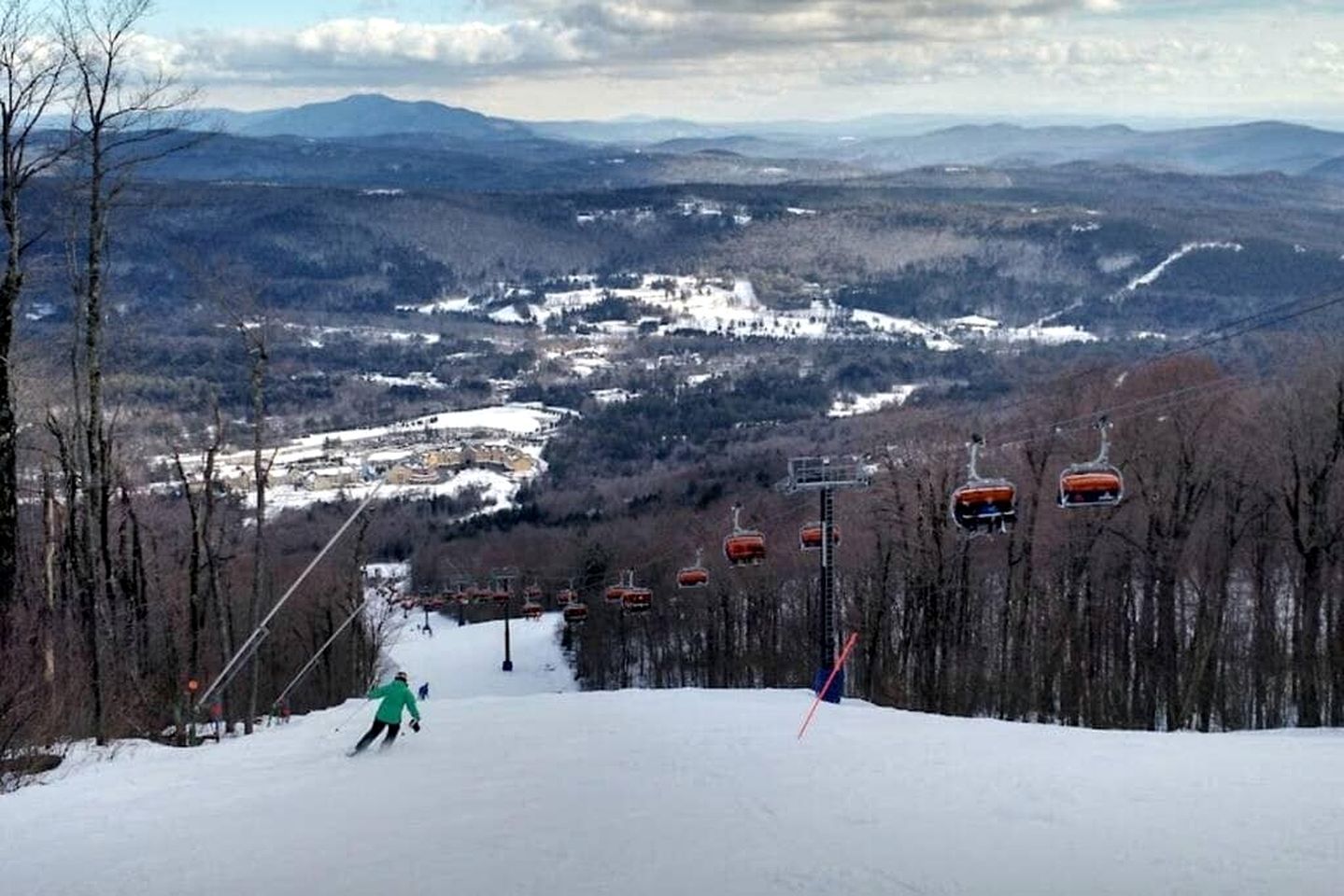 A ski slope with a chairlift, trees, and a distant town.