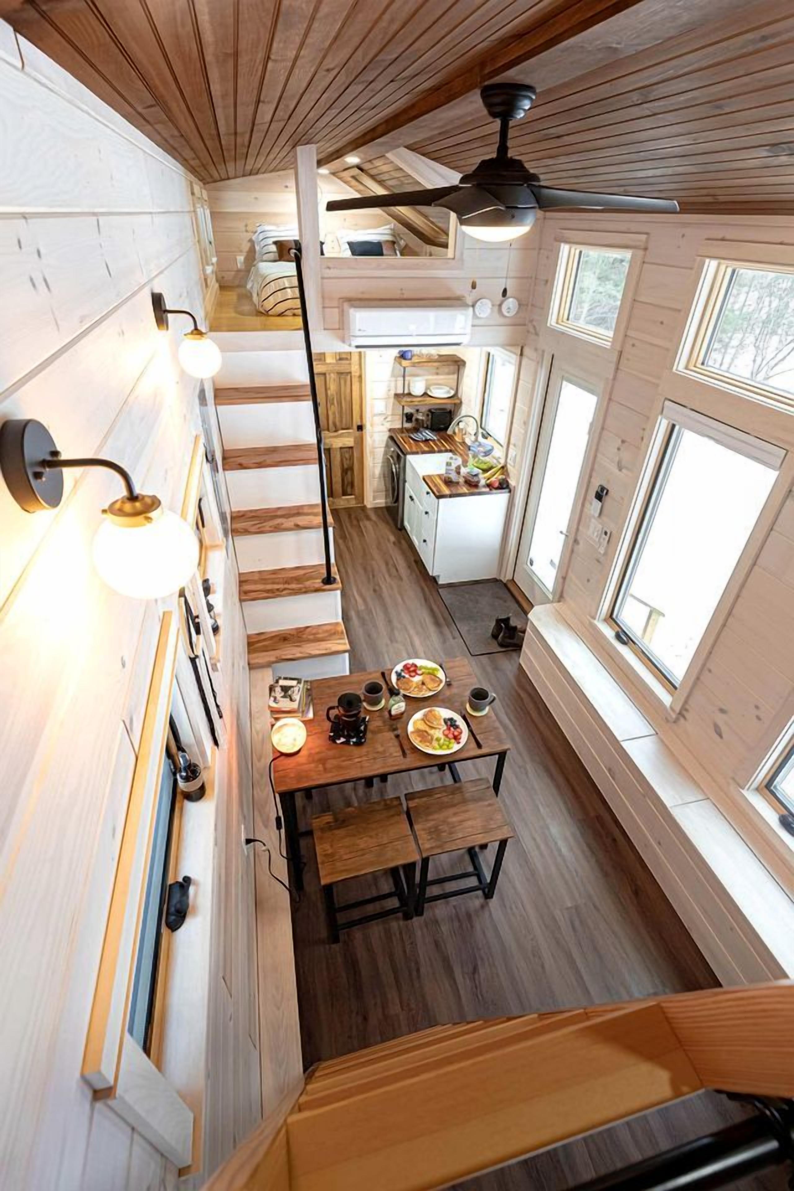 Une petite cabane en bois à plusieurs niveaux, comprenant une cuisine, un coin repas et un escalier.