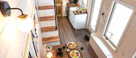Une petite cabane en bois à plusieurs niveaux, comprenant une cuisine, un coin repas et un escalier.
