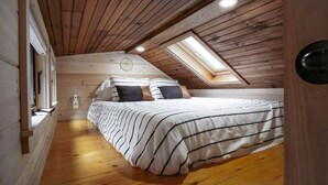 A bedroom with a sloped ceiling, wooden walls, a skylight, a bed with striped bedding, and a bedside table. - Gorgeous Cedar Tiny House for a Unique Pet-Friendly Getaway in Chester, Vermont (Chester)