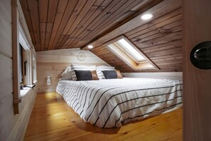 A bedroom with a sloped ceiling, wooden walls, a skylight, a bed with striped bedding, and a bedside table. - Gorgeous Cedar Tiny House for a Unique Pet-Friendly Getaway in Chester, Vermont (Chester)