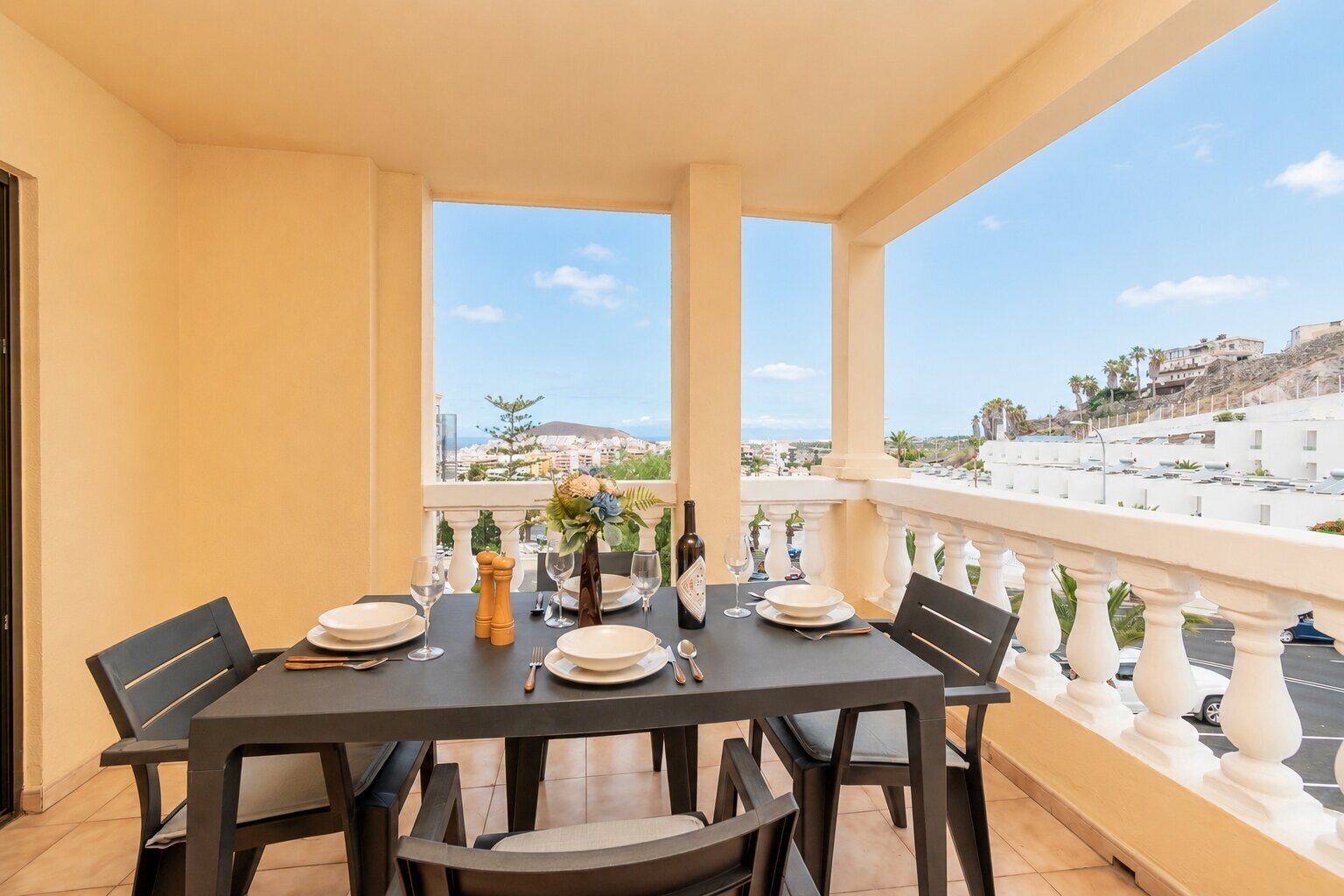 A balcony with a table set for two, overlooking a coastal cityscape.