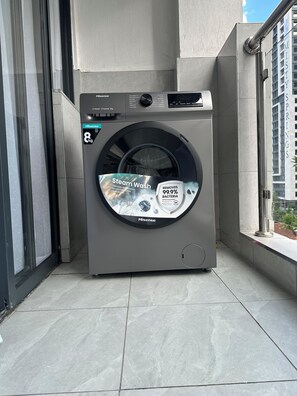 A Hisense 8kg front-loading washing machine on a balcony with a view of a building labeled 'MISTYS SPRINGS'. - Modern 1 bedroom in Westlands near GTC|wi-fi|gym (Nairobi)