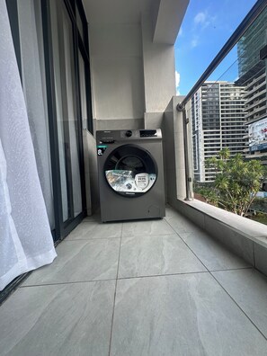 A Hisense 8kg front-loading washing machine on a balcony with a view of a building and some greenery. - Modern 1 bedroom in Westlands near GTC|wi-fi|gym (Nairobi)
