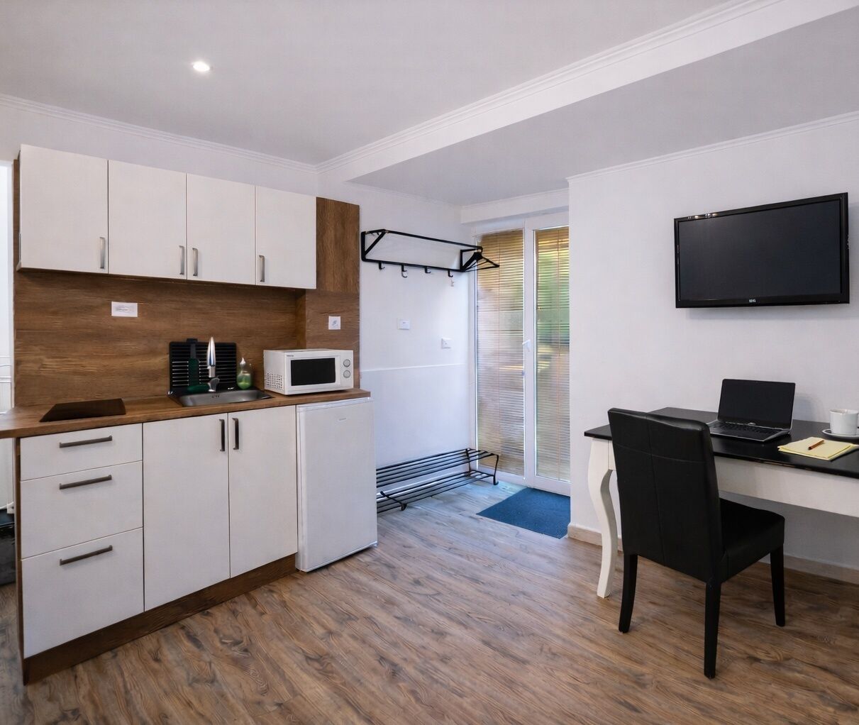 A compact kitchen with white cabinets, a microwave, and a black chair.