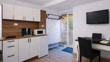 A compact kitchen with white cabinets, a microwave, and a black chair.