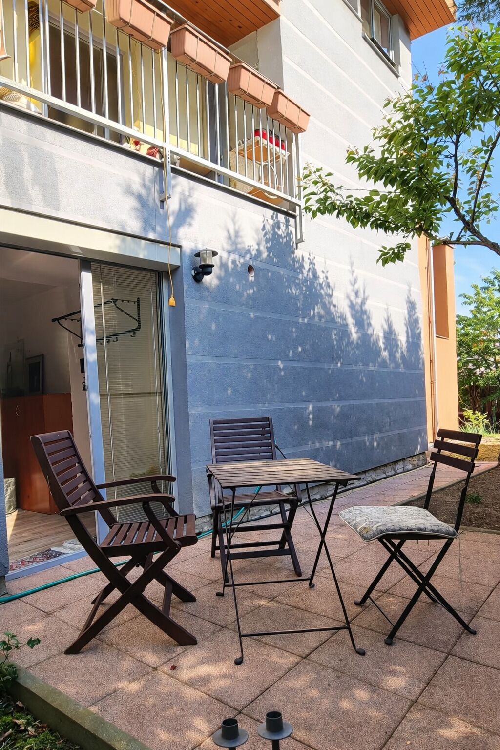 Eine Terrrasse im Freien mit Tisch und Stühlen, einer Schiebetür und einem Balkon mit Geländer.