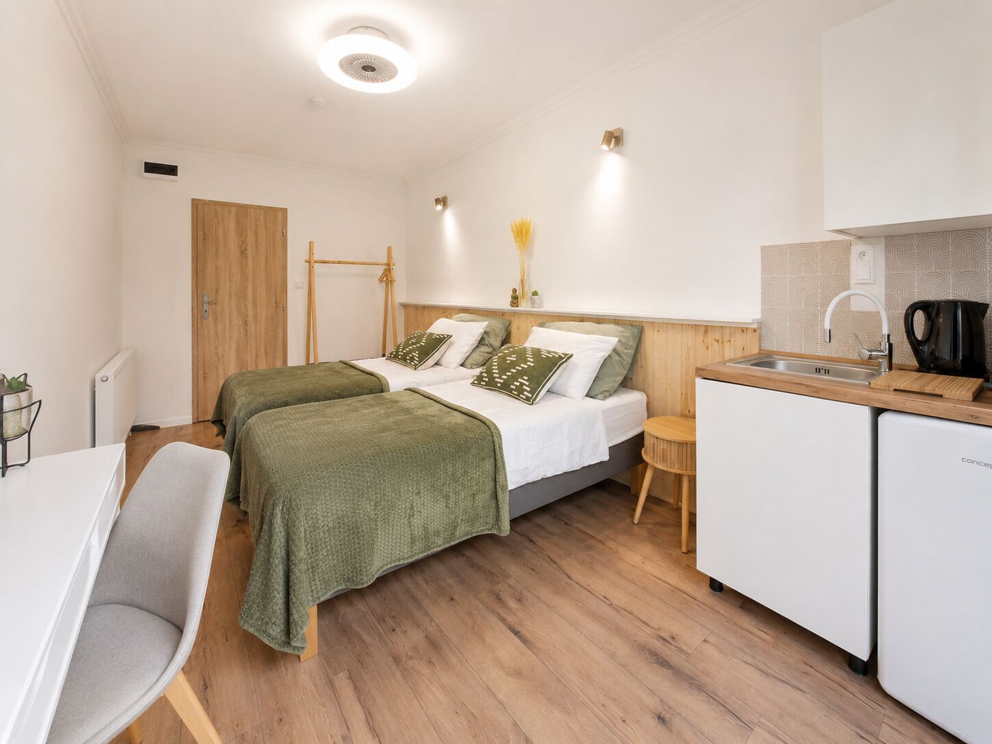 Une petite chambre moderne comprenant un lit, un bureau, une chaise, une petite table et un coin cuisine.