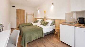 Une petite chambre moderne comprenant un lit, un bureau, une chaise, une petite table et un coin cuisine.