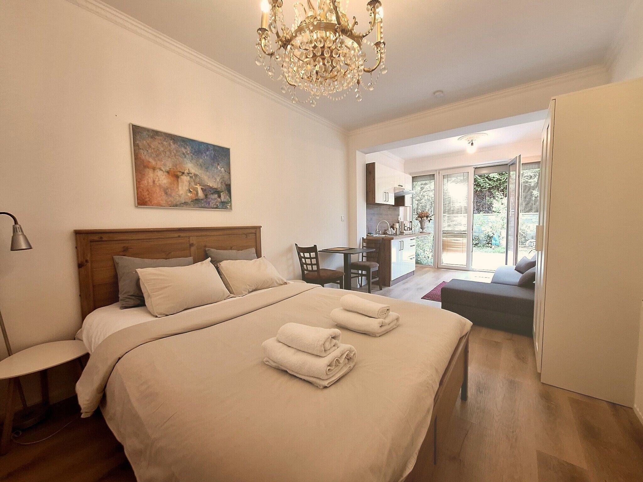 Een slaapkamer met een bed, een bureau en een stoel. Daarboven hangt een kroonluchter en aan de muur een schilderij.