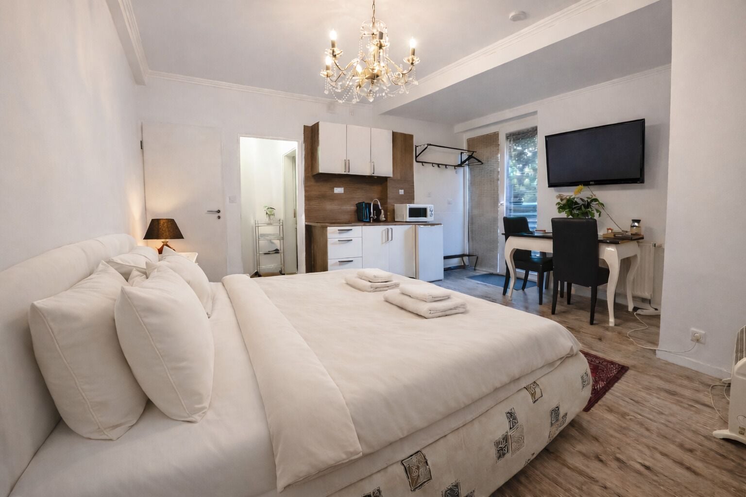 Un dormitorio con una cama grande, un escritorio, una silla, un televisor y una kitchenette.