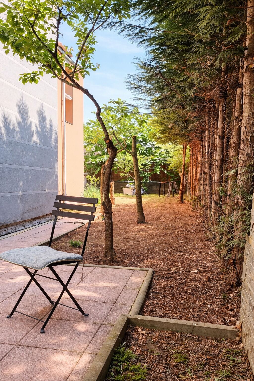 Un patio con un banco, un sendero arbolado y una pared de ladrillo.