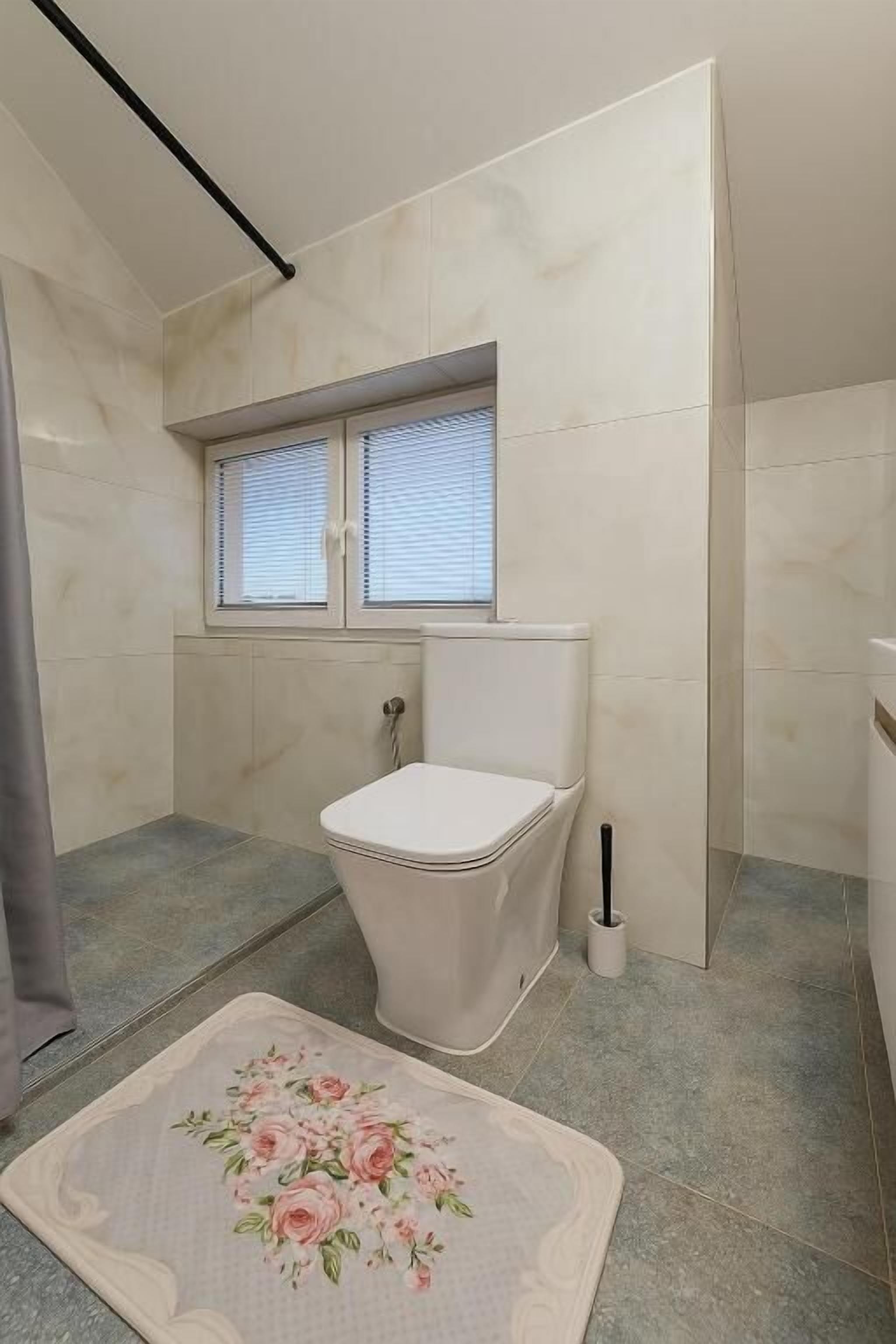 A bathroom with a toilet, a window, and a shower area.