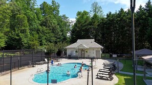 Ein Swimmingpool mit Liegestühlen, ein kleines Gebäude und ein eingezäunter Bereich.