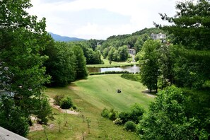 Ein Golfplatz mit Teich, umgeben von dichter Baumvegetation und einem Gebäude im Hintergrund.