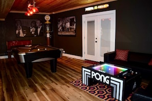 Ein Billardtisch mit Neon-Pong-Tisch in einem Raum mit Holzboden, einer Couch und einer Tür mit einem Schild darüber.
