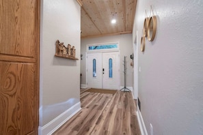 Un couloir avec un plancher en bois, une porte blanche ornée d’un vitrail et un porte-manteau.