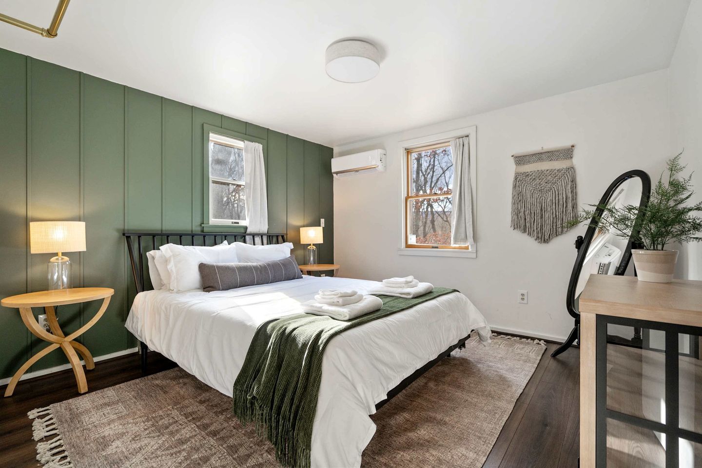 A bedroom with a bed, bedside tables, a mirror, a potted plant, and a window.