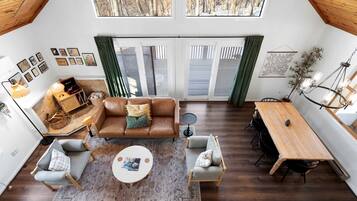 Ein geräumiger Loft mit hohen Decken, ein gemütlicher Wohnbereich mit einem braunen Ledersofa, einem Esstisch und einem großen Fenster mit Blick auf eine verschneite Landschaft.