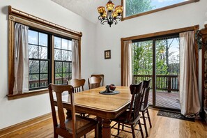 A dining room with a wooden table and chairs, large windows, and a chandelier. - Mountain Lodge with Hot Tub & Fire Pit in Berkeley Springs, West Virginia (Berkeley Springs)