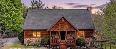 A log cabin with a stone foundation, a porch, and a chimney.