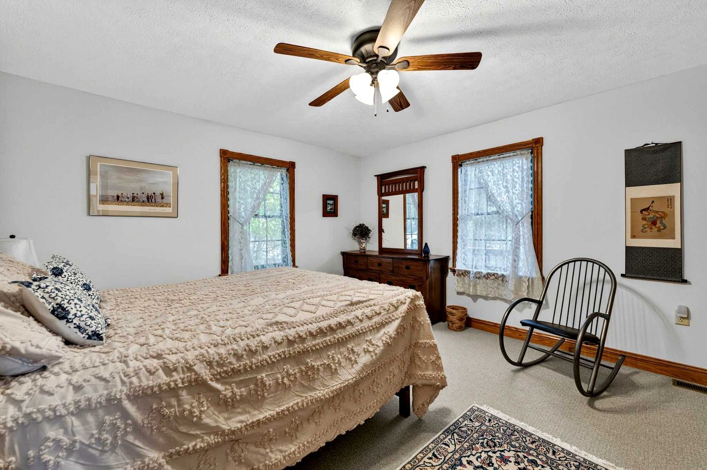 A bedroom with a bed, dresser, chair, and a ceiling fan.