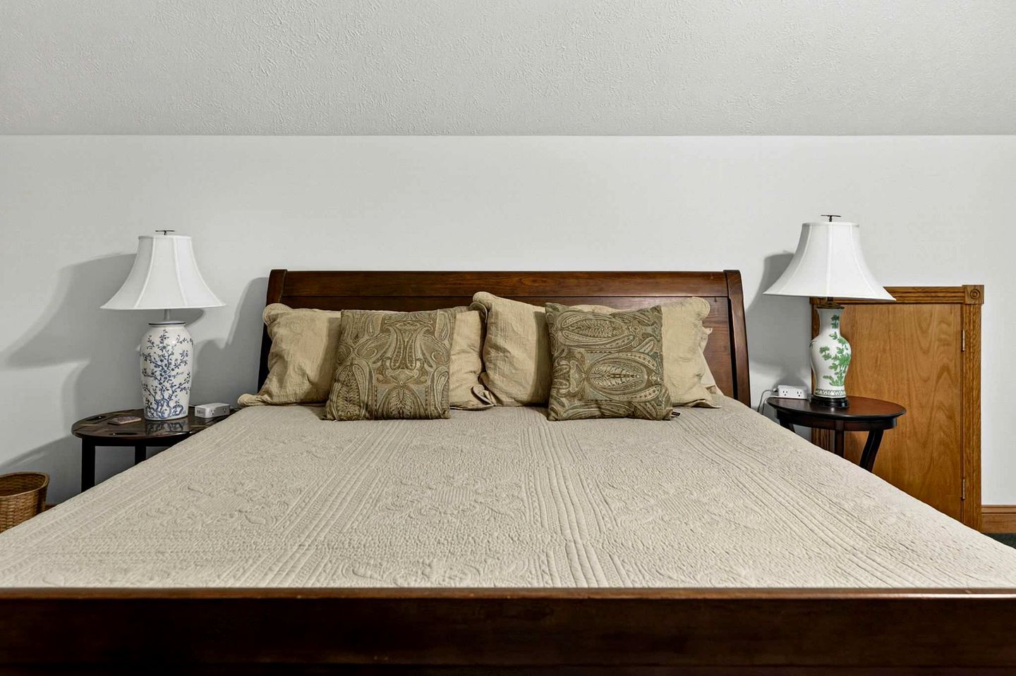 Ein Bett mit Holz-Kopfteil, zwei Nachttische mit Lampen und drei Zierkissen.