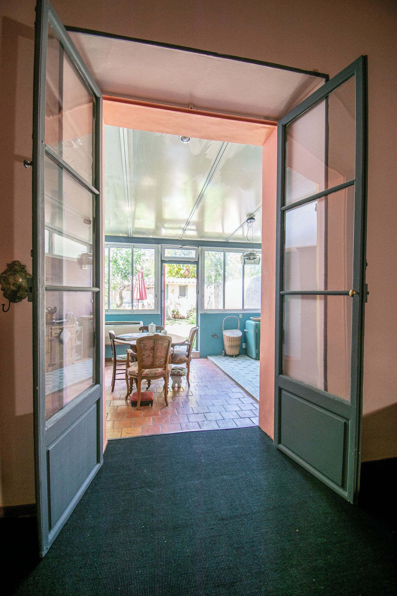 A hallway leading to a dining area with a table and chairs, a basket, and a door with glass panels.