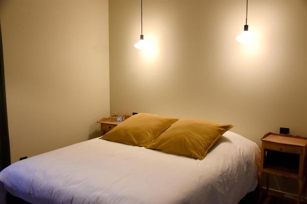 A bed with white bedding and two pillows, a bedside table with a radio, and a hanging light fixture.