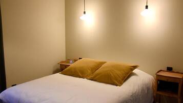 A bed with white bedding and two pillows, a bedside table with a radio, and a hanging light fixture.