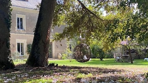 A garden with trees, a swing, and a building in the background.