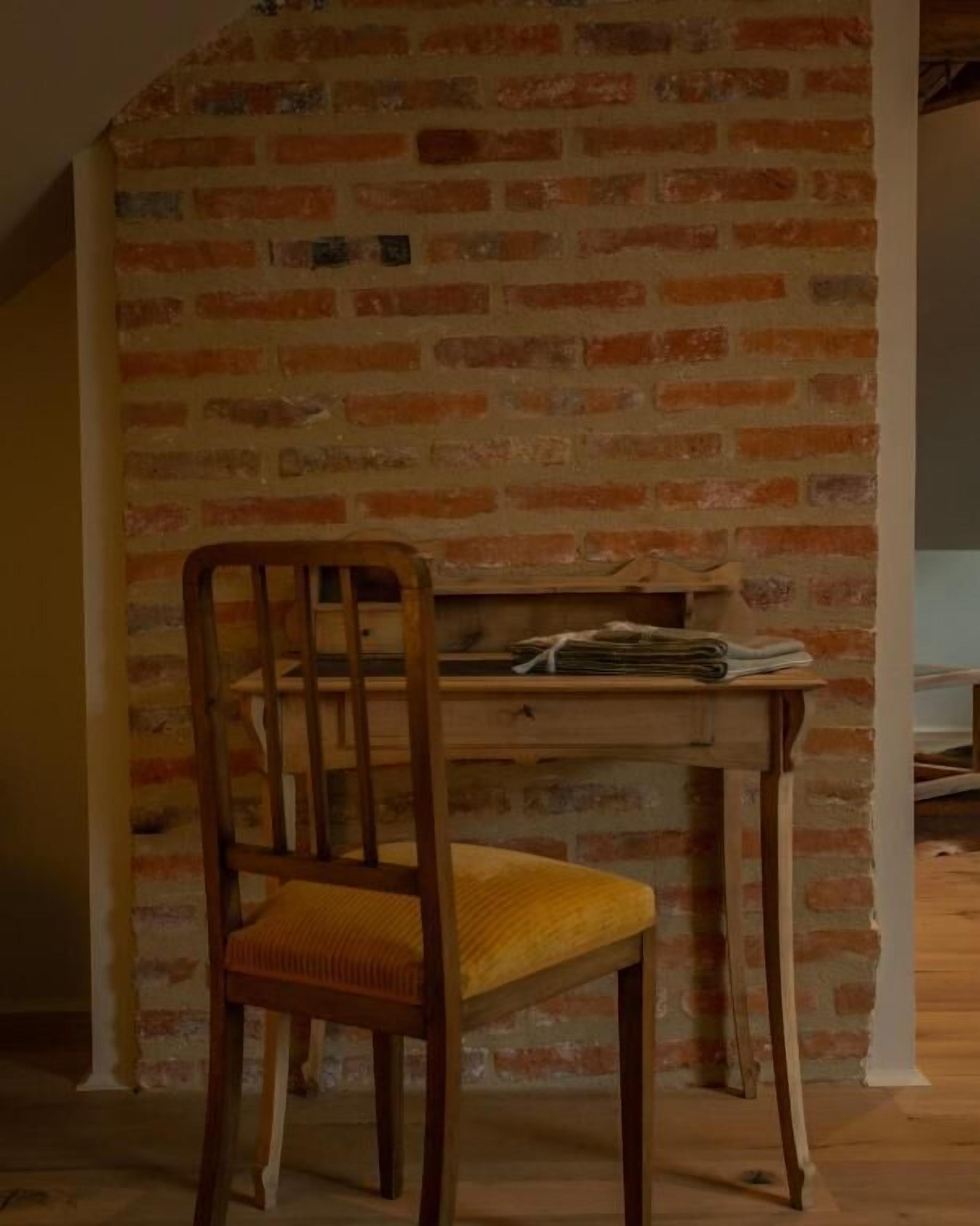Une chaise en bois avec un coussin, placée devant un mur de briques.