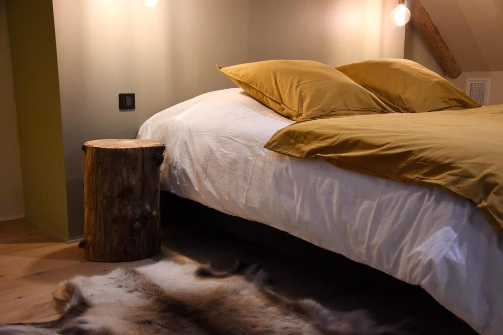 A bed with white bedding and two yellow pillows, a wooden stump, and a fur rug on the floor.