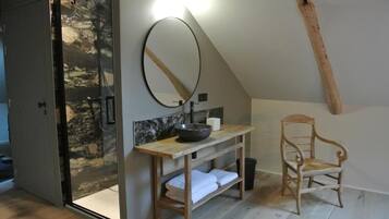 Un baño con tocador de madera, un espejo, lavamanos y una silla.